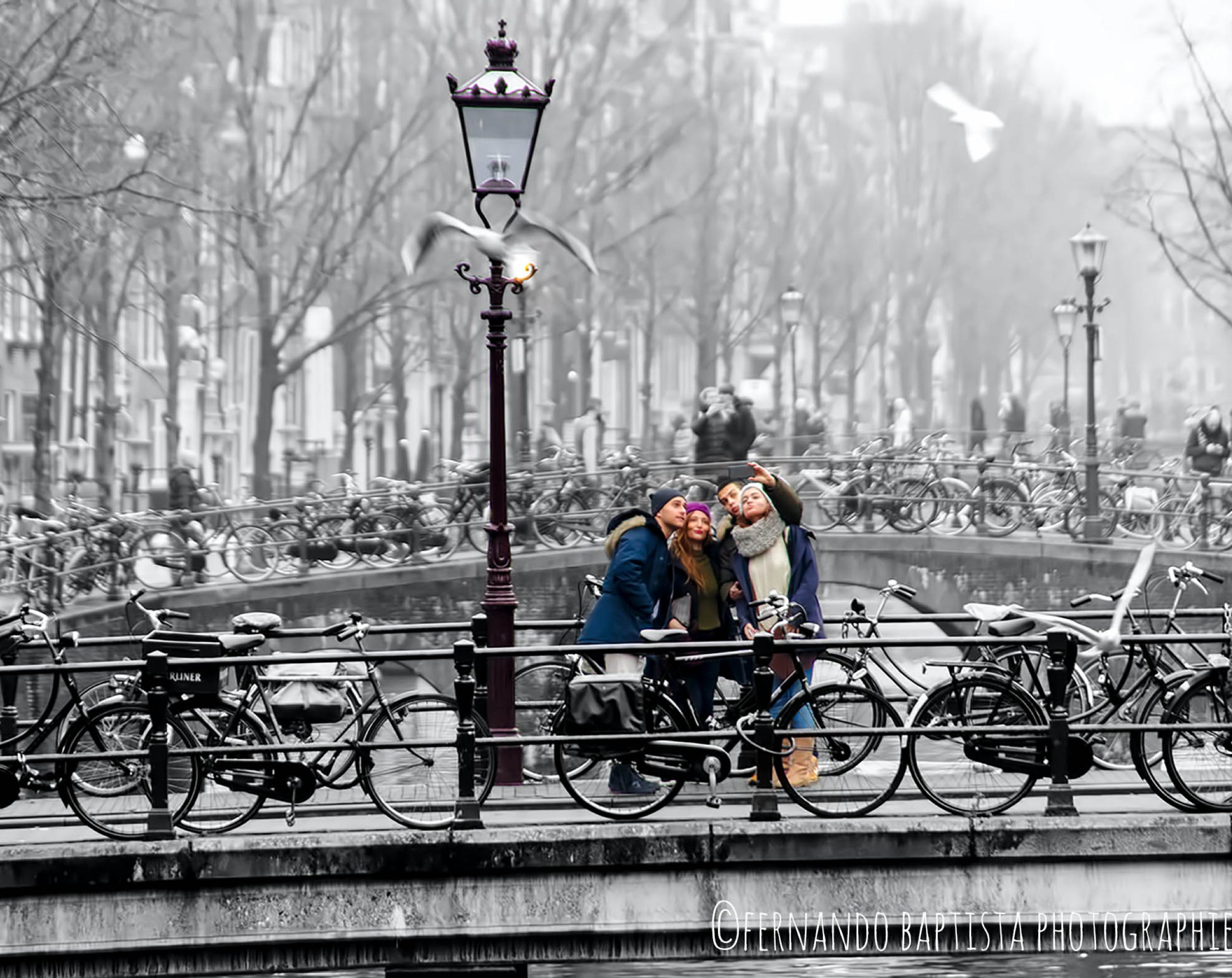 Vier junge Leute auf einer Brücke in Amsterdam machen Selfie.