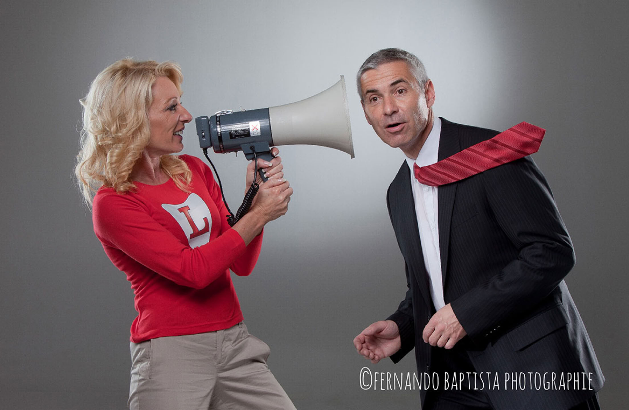 Frau spricht durch Megaphon und bläst einem Mann die Krawatte weg.