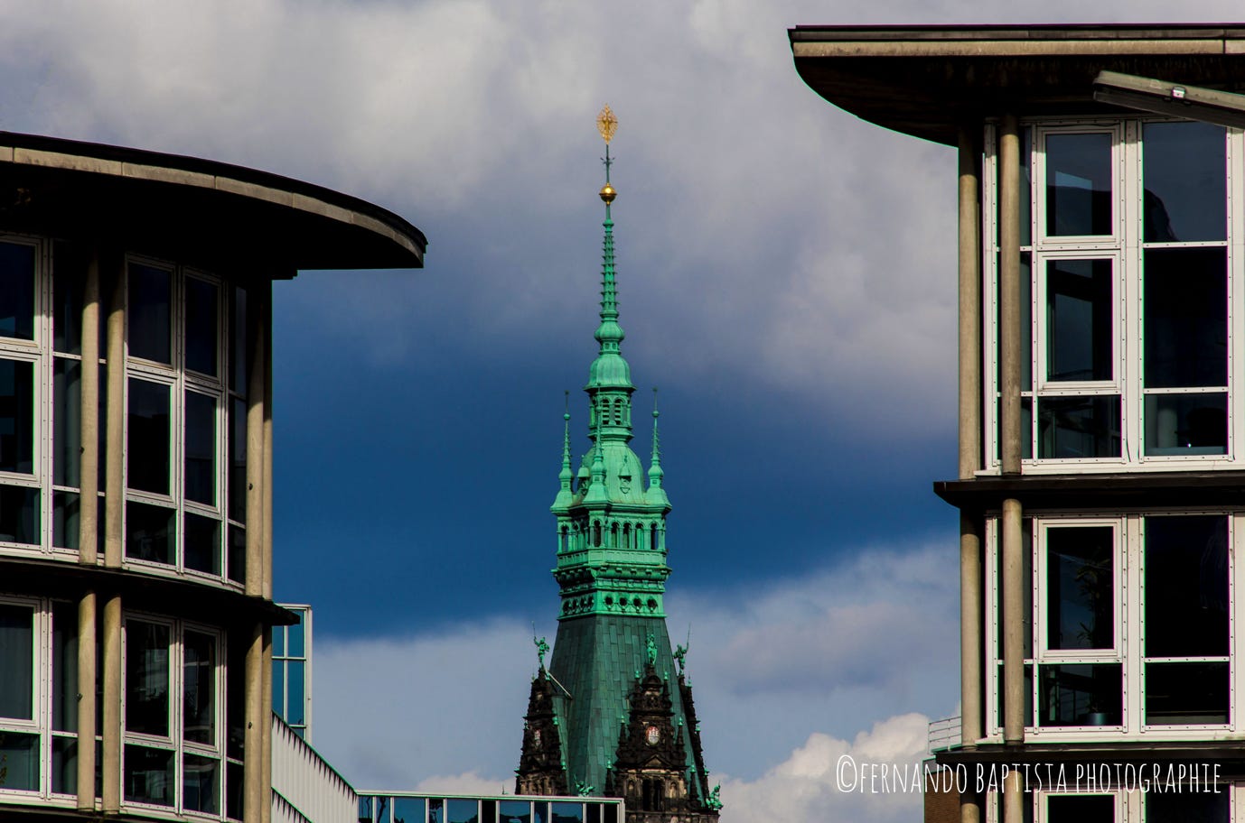 Rathaus-Turmspitze in Hamburg zwischen zwei Gebäuden.