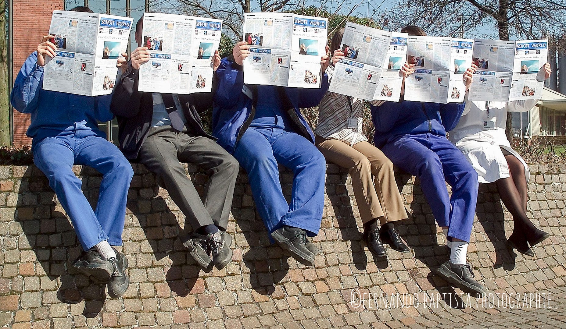 Sechs Menschen sitzen auf einer Mauer und lesen Zeitung